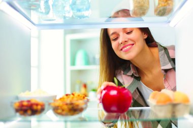 Sağlıklı yiyecek, sebze ve meyvelerle dolu açık buzdolabının yanında duran kadın portresi..
