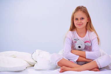 Küçük kız yatak odasında yatağın üzerine oturuyor. Küçük kız yatakta oturuyor ve bir pijama giymiş
