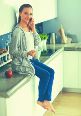 modern mutfakta otururken cep telefonu kullanan kadın.