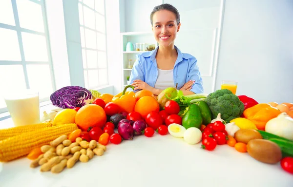 Stock image Young and cute woman sitting at the table full of fruits and vegetables in the wooden interior.