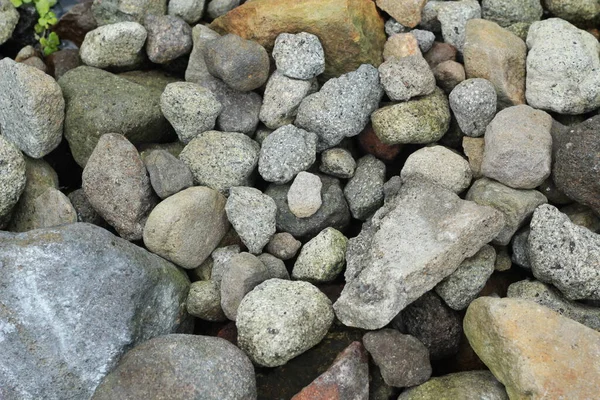 Natural rocks on the river bank. Pebbles and colored pebbles in water close-up. Texture of mixed different sizes stones on the shore of the river bank.
