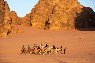 Ürdün, Wadi Rum - 2 Kasım 2022: Çölde turist taşıyan develer kervanı, gün batımında kaya dağları