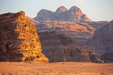 Ürdün, Wadi Rum - 2 Kasım 2022 Çölde develerin karavanı, gün batımında kaya dağları