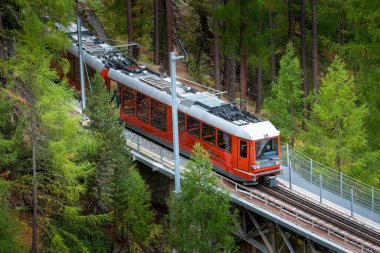 Zermatt, İsviçre - 7 Ekim 2019: Gornergrat köprüdeki kırmızı turist treni, köy evleri ve İsviçre Alpleri panoraması