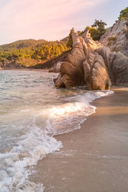 Vourvourou, Chalkidiki veya Halkidiki, Yunanistan 'ın Turkuaz denizi, orman yeşili dağlar ve Fava kumsalındaki kayalıklarla yaz günbatımı manzarası
