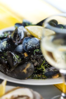 Tabakta beyaz şarap soslu midye ve çözülmüş şarap kadehi.