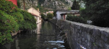 Karadağ 'ın Kotor kentinde yaz aylarında kanal boyunca uzanan renkli dar sokaklar, evler ve ağaçlar, afişler