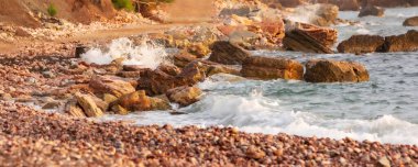 Karadağ 'daki Crvena Glavica plajı. Kırmızı kayalar kıyılar ve su dalgaları, bayrak