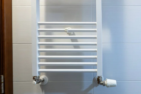 White electric towel dryer for the bathroom mounted on a wall with tiles