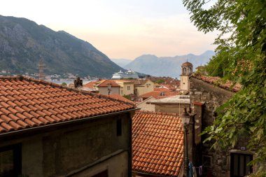 Kotor, Karadağ - 20 Eylül 2023: Eski şehir tarihi kulesi ve evleri, büyük yolcu gemisi günbatımı manzarası