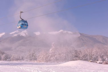 Bansko, Bulgaristan - 5 Aralık 2019: Mavi gondol asansör kulübeleri, orman çam ağaçları, Pirin dağı zirveleri manzaralı ve yamaçlı kış kayak merkezi manzarası