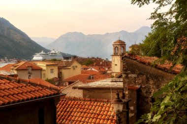 Kotor, Karadağ - 20 Eylül 2023: Eski şehir tarihi kulesi ve evleri, büyük yolcu gemisi günbatımı manzarası