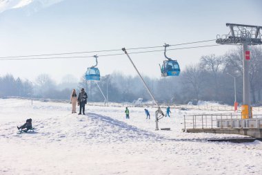 Bansko, Bulgaristan - 20 Aralık 2023: Gondol kaldırma kulubeleri, Pirin dağ zirveleri manzaralı Bulgar kış kayak merkezi manzarası ve daha düşük istasyon yakınlarındaki insanlar