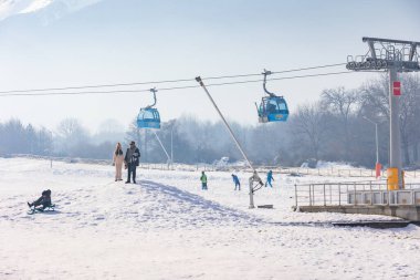 Bansko, Bulgaria - December 20, 2023: Bulgarian winter ski resort panorama with gondola lift cabins, Pirin mountain peaks view and people near lower station clipart