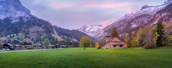 stock image St. Mary Church, Kandersteg, Canton of Bern, Switzerland, Europe, autumn trees and sunset snow mountains panoramic banner