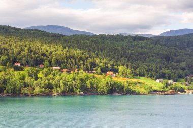 Norveç köyünün yaz manzarası turkuaz fiyort suyu, dağlar ve renkli evlerle. Olden, Norveç