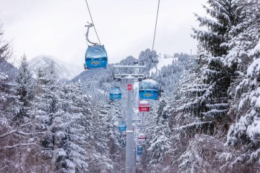 Bansko, Bulgaristan - 21 Ocak 2024: Mavi gondol asansör kulübeleri, kar ormanı çam ağaçları, dağ zirveleri manzaralı kış kayak merkezi manzarası