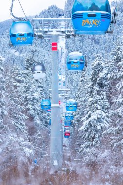 Bansko, Bulgaristan - 21 Ocak 2024: Mavi gondol asansör kulübeleri, kar ormanı çam ağaçları, dağ zirveleri manzaralı kış kayak merkezi manzarası