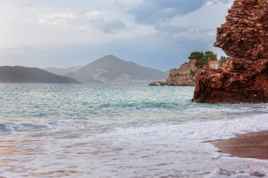 Hotel on the island of Sveti Stefan at sunset, near Budva, Montenegro. Waves and red rocks clipart