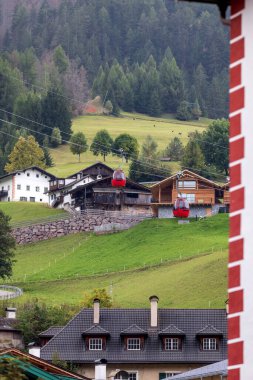 Ortisei, Italy summer view in alpine village in Dolomites with Mont Seuc cable car red cabins and houses clipart