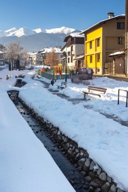 Bansko, Bulgaristan - 18 Ocak 2025: Gotse Delchev sokak manzaralı eski, geleneksel evler, su deresi ve kışın Pirin dağları