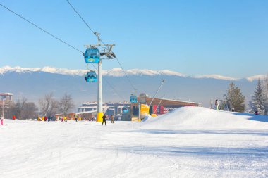 Bansko, Bulgaristan - 17 Ocak 2025: Gondol kaldırma kulubeleri, dağ zirveleri manzaralı Bulgar kış kayak merkezi manzarası ve daha düşük istasyon yakınlarındaki kayakçılar