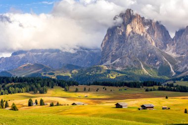 Dolomitler, Alpe di Siusi veya Seiser Alm 'deki geleneksel ahşap kulübelerle yeşil kayan tepelerin panoramik manzarasına sahipler.