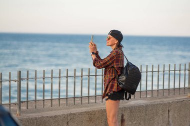 Güzel kadın turist, altın günbatımı saatinde akıllı telefonuyla fotoğraf çekiyor.