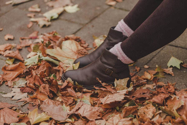 Женщина, сидящая в осеннем парке в осенних бежевых и коричневых тонах, крупным планом на ногах