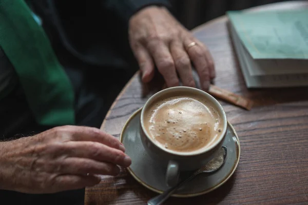 hands of a old person wearing suit and drinking coffee in a cafe