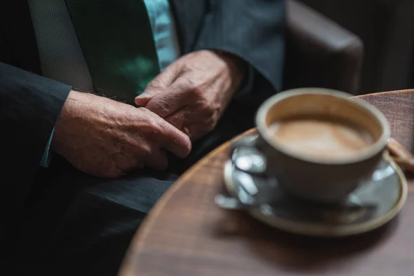一个穿着西服在咖啡店喝咖啡的老人的手 免版税图库照片