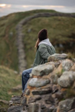 Woman tourist with Hadrian's wall on the background, happy Traveler travel Northumberland, United Kingdom. Destination and Vacation clipart