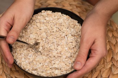 Oats Trickling from Hand into Bowl. Hand sprinkling rolled oats into a black bowl clipart