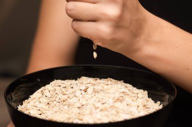 Oats Trickling from Hand into Bowl. Hand sprinkling rolled oats into a black bowl clipart