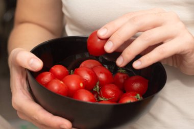 Holding a Bowl of Cherry Tomatoes. Hands cradling a black bowl filled with bright red cherry tomatoes clipart