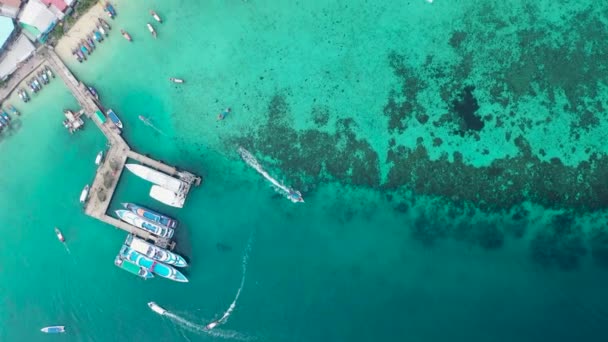 カラフルなタイの伝統的なロングテールボートの空中トップダウンドローンビューは ファイ島で透明な青い海の水と桟橋で1行に駐車しました — ストック動画