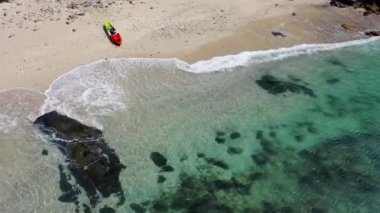 Aeial view of crystal clear beach with a kayak parked on white sand.