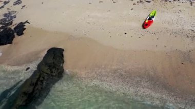 Aeial view of crystal clear beach with a kayak parked on white sand.