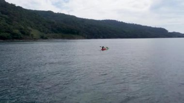 Sea kayaking. Tracking shot of kayaker paddling green and orange touring kayak. Rear view of man paddling green and orange sea kayak.
