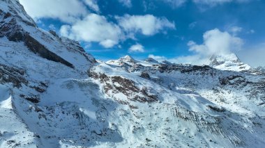 Gorgeus karlı dağ sırası ve karlı zirvede çığ duvarları. Yarı bulutlu, yarı güneşli bir gün. Dağın tepesinden bak.