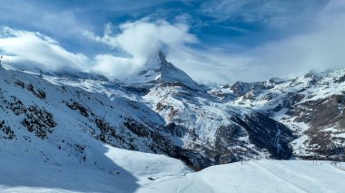 Güneşli bir günde karlı Matterhorn zirvesinin manzarası mavi gökyüzü ve arka planda dramatik bulutlar, İsviçre.