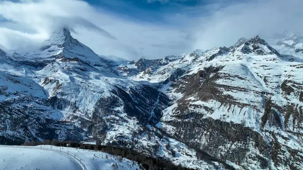 Gorgeus karlı dağ sırası ve karlı zirvede çığ duvarları. Yarı bulutlu, yarı güneşli bir gün. Dağın tepesinden bak.