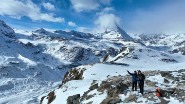 Genç Asyalı adamın panoramik manzarası ve arkadaşı ünlü Gornergrat gözlemevinin tepesinde uzaktan kumandayla çalışıyor. İkonik ünlü Matterhorn geçmişi. İsviçre, İsviçre.