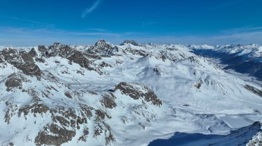 Tepeleri karla kaplı dağlık arazi ve bulutsuz mavi gökyüzü.