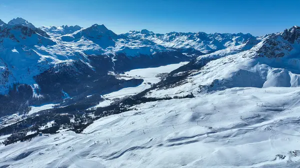 Açık mavi gökyüzü olan karlı bir dağ manzarası ve ön planda yükselen kayak kaldırma koltukları.
