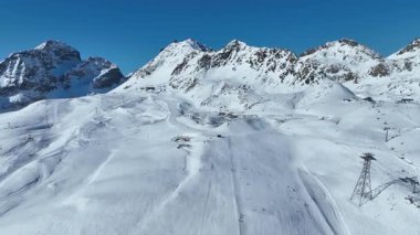 Mavi gökyüzü ve teleferik teleferiğiyle karlı dağ tepesi vadisinde hava manzarası. Kışın turist kayağı taşımacılığı. Kışın yüksek irtifa gondolu. Kayak merkezi Engadin.
