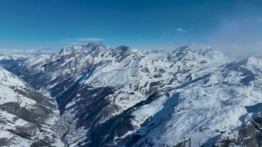 Zermatt 'taki karlı kış vadisinde dönen sinematik sakin dron görüntüsü. İsviçre 'deki dağların arasında İsviçre Alpleri köyü. Berrak mavi gökyüzüyle göz kamaştırıcı bir dağ manzarası.