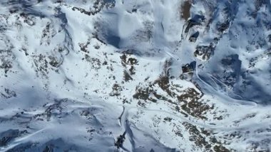 Kayakçılar karlı yamaçlarda güneşli bir günün tadını çıkarıyorlar ve arka planda İsviçre 'de teleferik var. Trockener Steg ve Schwarzsee 'nin kayak merkezi Zermatt' ta.
