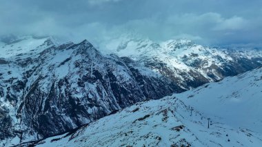 İsviçre 'deki Zermatt kayak merkezindeki karlı alp manzarası, bakımlı bir patikada kayakçılar, kayak kaldırma tesisleri ve güneşli bir tepe noktası.