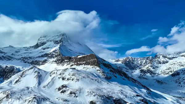 İsviçre 'deki Zermatt kayak merkezinin manzarasında açık mavi gökyüzü altında Matterhorn, kayak asansörleri, karla kaplı yamaçlar ve engebeli alp zirveleri görülüyor..
